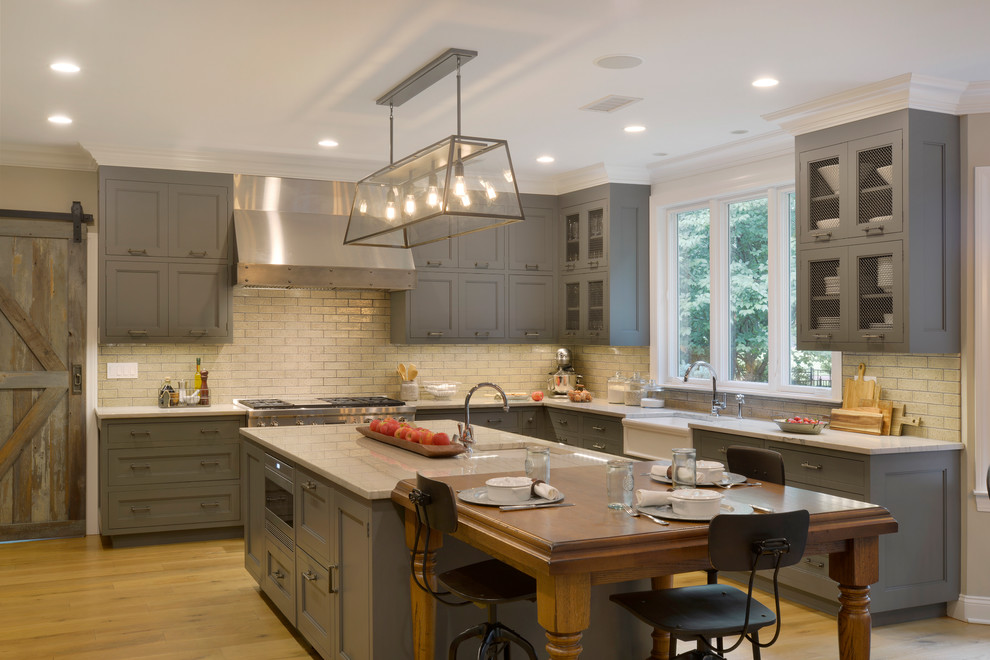 Expansive country u-shaped kitchen/diner in New York with a belfast sink, recessed-panel cabinets, grey cabinets, quartz worktops, stainless steel appliances, light hardwood flooring, an island, beige floors, white splashback and white worktops.