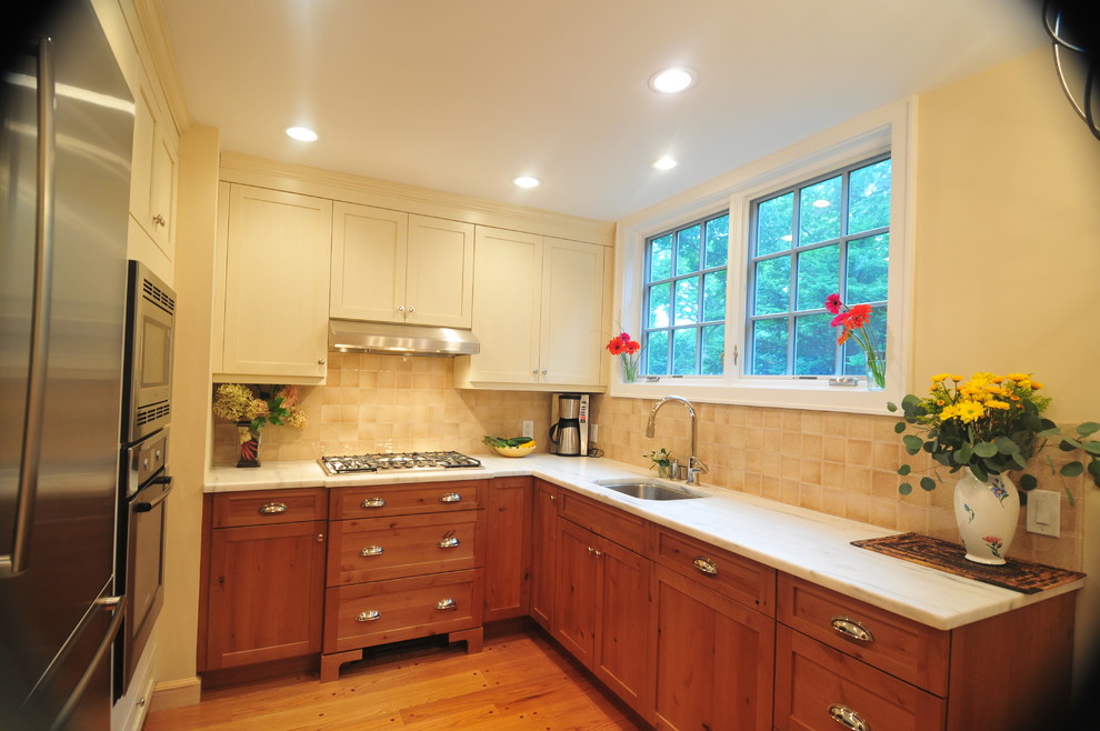 Inspiration for a mid-sized transitional u-shaped light wood floor kitchen remodel in New York with an undermount sink, shaker cabinets, medium tone wood cabinets, marble countertops, beige backsplash, ceramic backsplash, stainless steel appliances and no island
