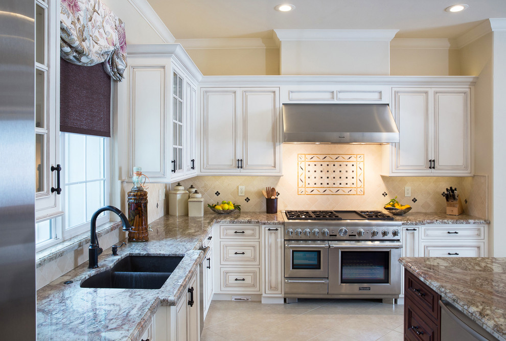 Klassisk inredning av ett stort l-kök, med en undermonterad diskho, luckor med upphöjd panel, vita skåp, beige stänkskydd, rostfria vitvaror, granitbänkskiva, en köksö och beiget golv