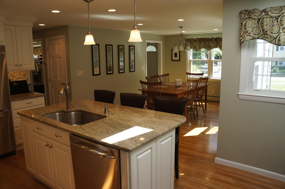 Inredning av ett klassiskt kök, med en undermonterad diskho, luckor med upphöjd panel, vita skåp, granitbänkskiva, rostfria vitvaror och en köksö