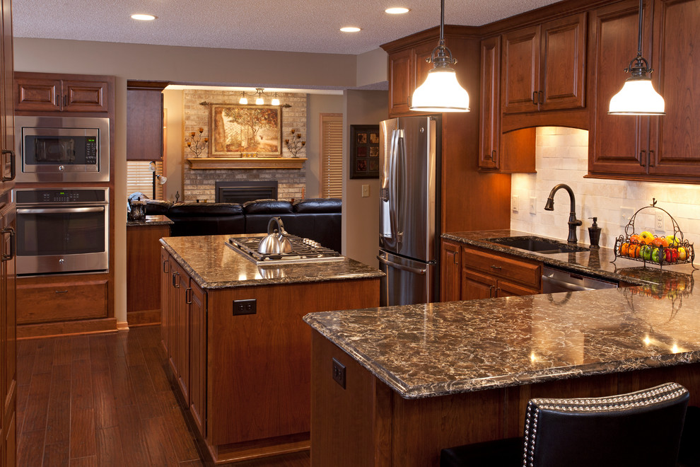 Mid-sized elegant l-shaped medium tone wood floor enclosed kitchen photo in Minneapolis with an undermount sink, raised-panel cabinets, medium tone wood cabinets, quartz countertops, beige backsplash, subway tile backsplash, stainless steel appliances and two islands