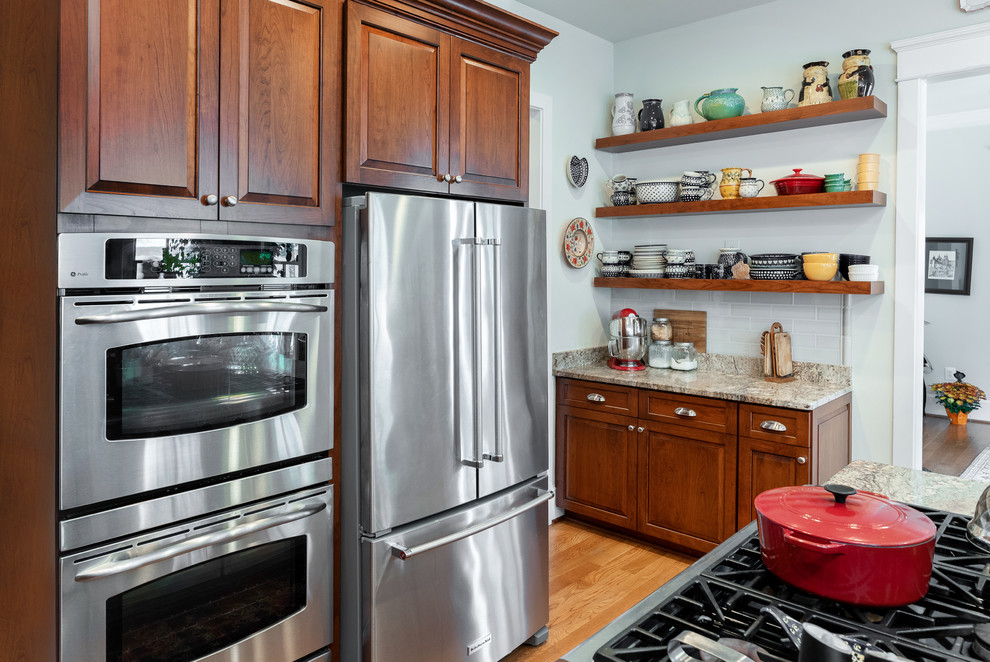 Example of a classic u-shaped eat-in kitchen design in DC Metro with an undermount sink, raised-panel cabinets, medium tone wood cabinets, granite countertops, stainless steel appliances and an island