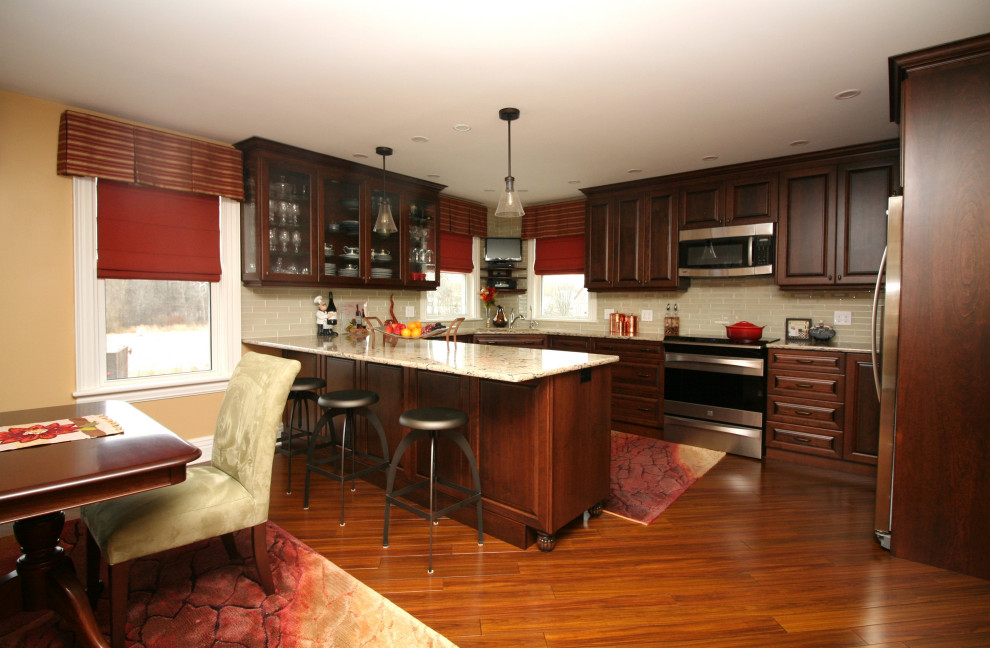Photo of a large classic u-shaped kitchen/diner in Other with a submerged sink, raised-panel cabinets, dark wood cabinets, engineered stone countertops, beige splashback, glass tiled splashback, stainless steel appliances, bamboo flooring, a breakfast bar, brown floors and beige worktops.