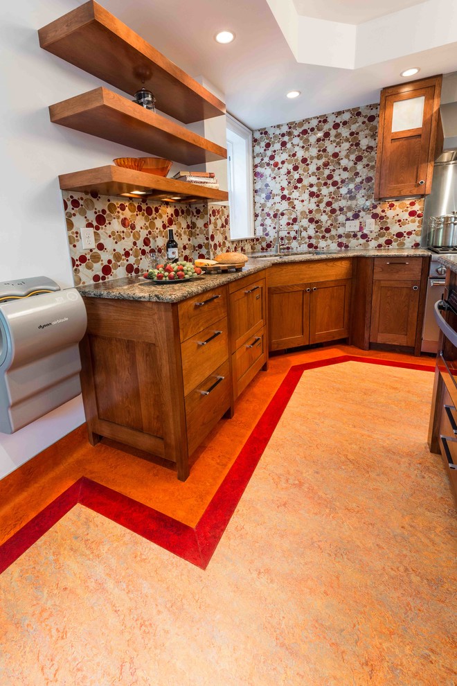 Inredning av ett modernt kök, med en dubbel diskho, luckor med infälld panel, skåp i mellenmörkt trä, granitbänkskiva, flerfärgad stänkskydd, rostfria vitvaror, linoleumgolv och en köksö