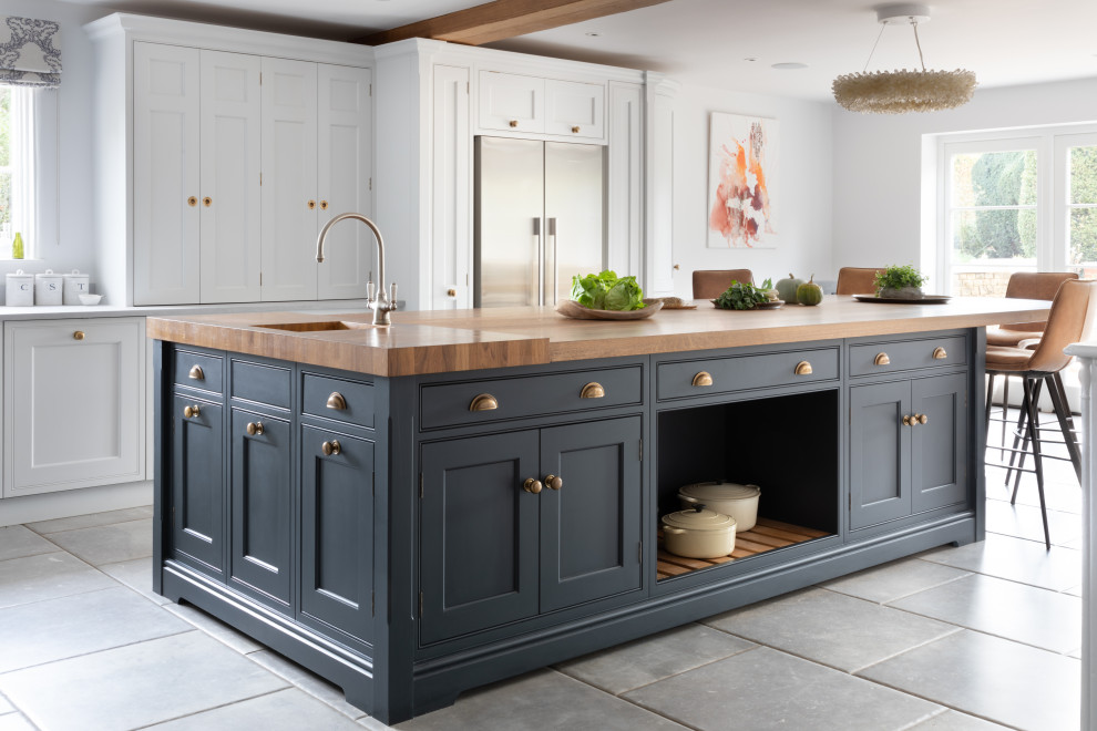 This is an example of a large traditional l-shaped kitchen/diner in Surrey with a built-in sink, shaker cabinets, white cabinets, wood worktops, blue splashback, glass sheet splashback, stainless steel appliances, porcelain flooring, an island, grey floors, brown worktops and exposed beams.