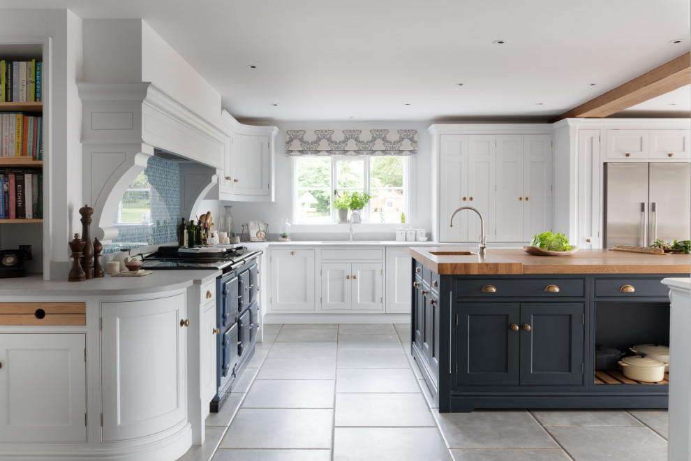 This is an example of a large traditional l-shaped kitchen/diner in Surrey with a built-in sink, shaker cabinets, white cabinets, wood worktops, blue splashback, glass sheet splashback, stainless steel appliances, porcelain flooring, an island, grey floors, brown worktops and exposed beams.