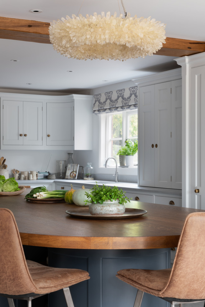 This is an example of a large classic l-shaped kitchen/diner in Surrey with a built-in sink, shaker cabinets, white cabinets, wood worktops, blue splashback, glass sheet splashback, stainless steel appliances, porcelain flooring, an island, grey floors, brown worktops and exposed beams.