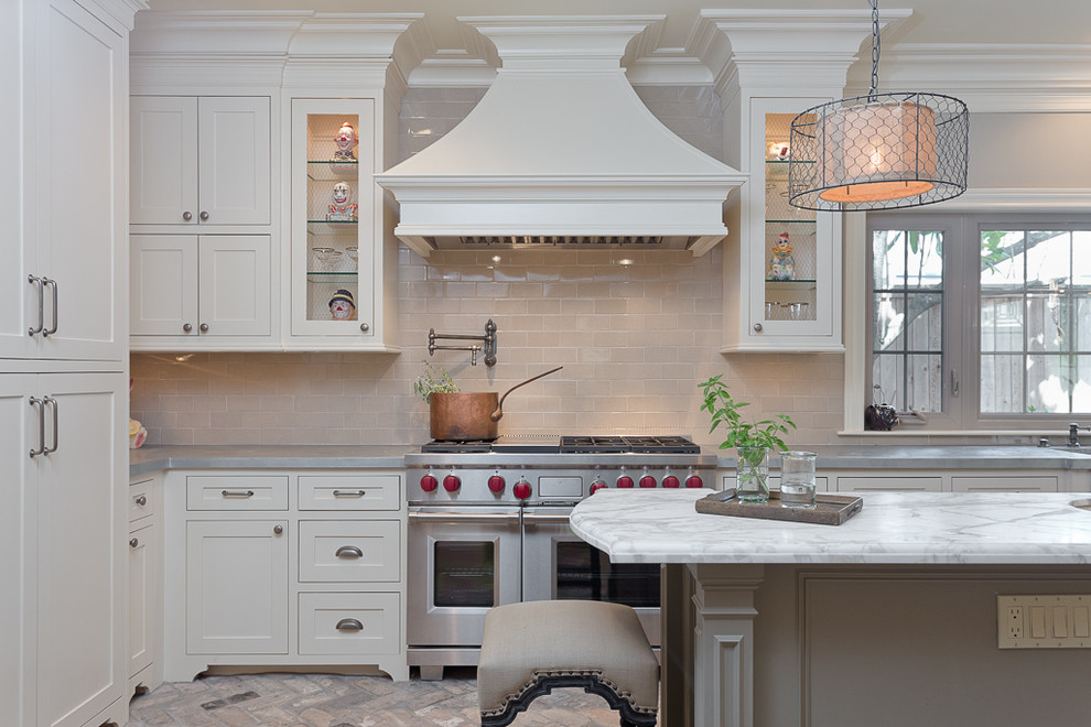 Inspiration for a medium sized traditional u-shaped open plan kitchen in Houston with a belfast sink, recessed-panel cabinets, white cabinets, zinc worktops, beige splashback, stainless steel appliances, brick flooring and an island.