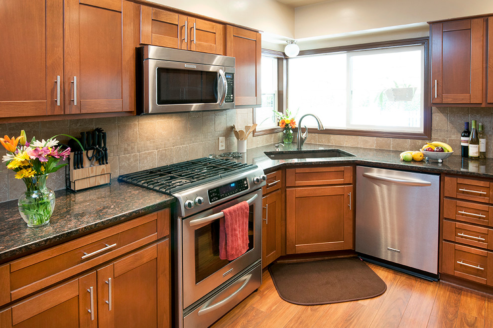 Exempel på ett avskilt, litet klassiskt l-kök, med en undermonterad diskho, skåp i shakerstil, skåp i mörkt trä, granitbänkskiva, beige stänkskydd, stänkskydd i stenkakel, rostfria vitvaror, mellanmörkt trägolv och brunt golv