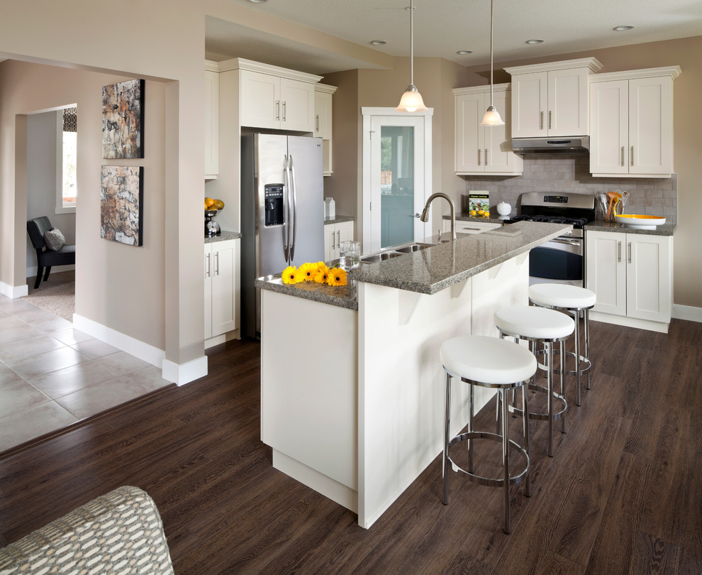 Elegant l-shaped open concept kitchen photo in Vancouver with a drop-in sink, shaker cabinets, white cabinets, granite countertops, gray backsplash, subway tile backsplash and stainless steel appliances