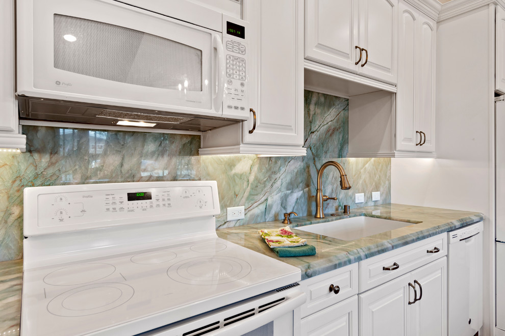 Example of a classic l-shaped brown floor eat-in kitchen design in Other with an undermount sink, raised-panel cabinets, white cabinets, quartzite countertops, green backsplash, stone slab backsplash, white appliances and green countertops