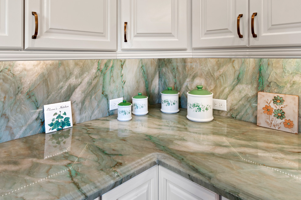 Inredning av ett klassiskt grön grönt kök, med en undermonterad diskho, luckor med upphöjd panel, vita skåp, bänkskiva i kvartsit, grönt stänkskydd, stänkskydd i sten, vita vitvaror och brunt golv