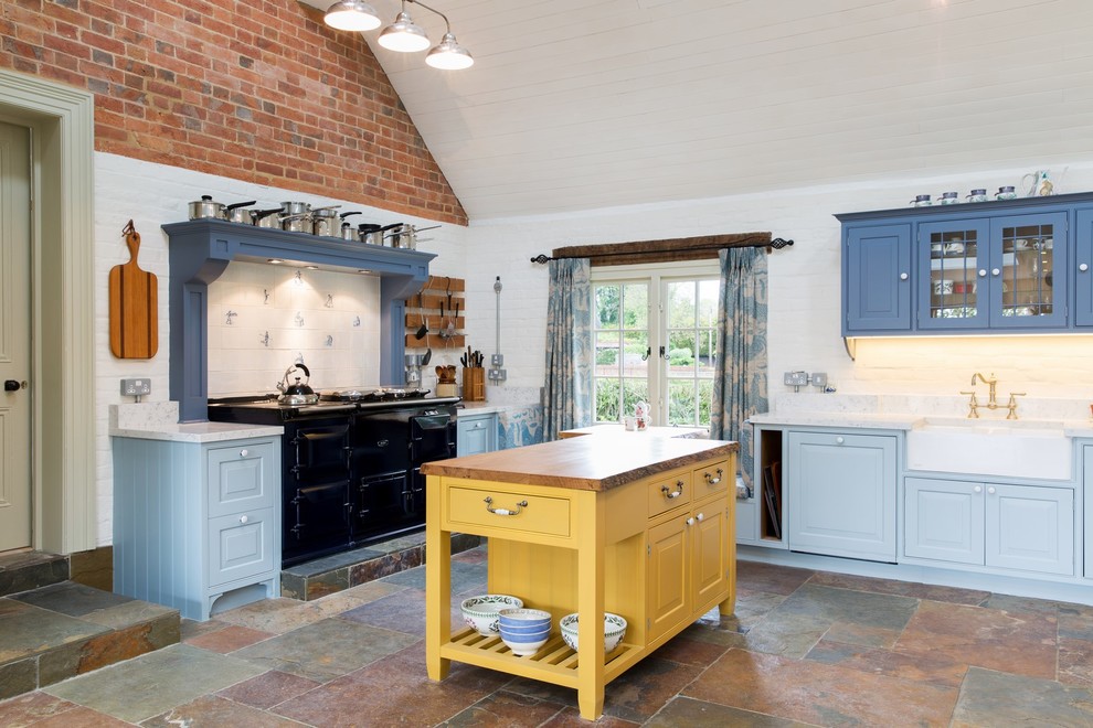 Idéer för att renovera ett vintage kök, med en rustik diskho, luckor med glaspanel, blå skåp, träbänkskiva, svarta vitvaror, skiffergolv, en köksö och flerfärgat golv