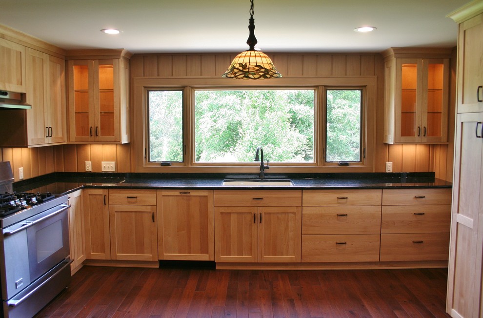Klassisk inredning av ett kök, med en undermonterad diskho, luckor med infälld panel, skåp i ljust trä, granitbänkskiva, integrerade vitvaror och mörkt trägolv