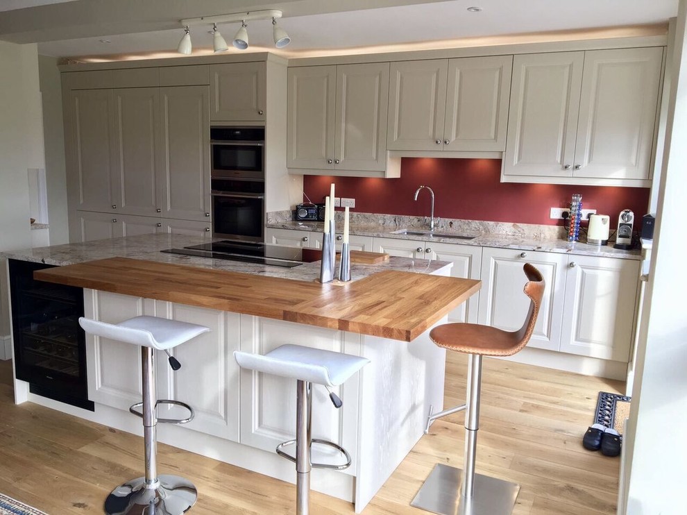 Offene, Große Klassische Küche mit Schrankfronten im Shaker-Stil, weißen Schränken, Granit-Arbeitsplatte, Elektrogeräten mit Frontblende, hellem Holzboden und Kücheninsel in Surrey