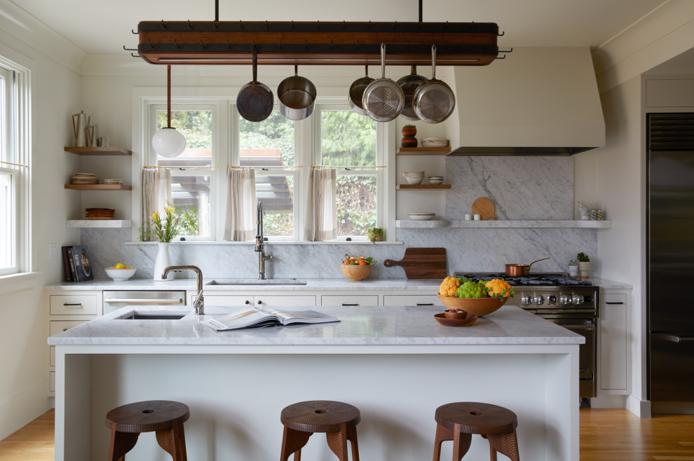 Klassische Küche mit Unterbauwaschbecken, flächenbündigen Schrankfronten, beigen Schränken, Küchenrückwand in Weiß, Rückwand aus Stein, Küchengeräten aus Edelstahl, braunem Holzboden, Kücheninsel und weißer Arbeitsplatte in Portland