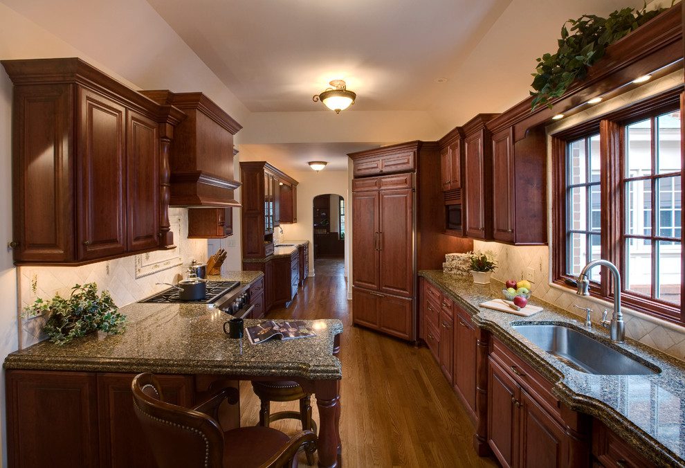 This is an example of a traditional galley kitchen/diner in Chicago with a submerged sink, raised-panel cabinets, dark wood cabinets, engineered stone countertops, beige splashback, stone tiled splashback and stainless steel appliances.