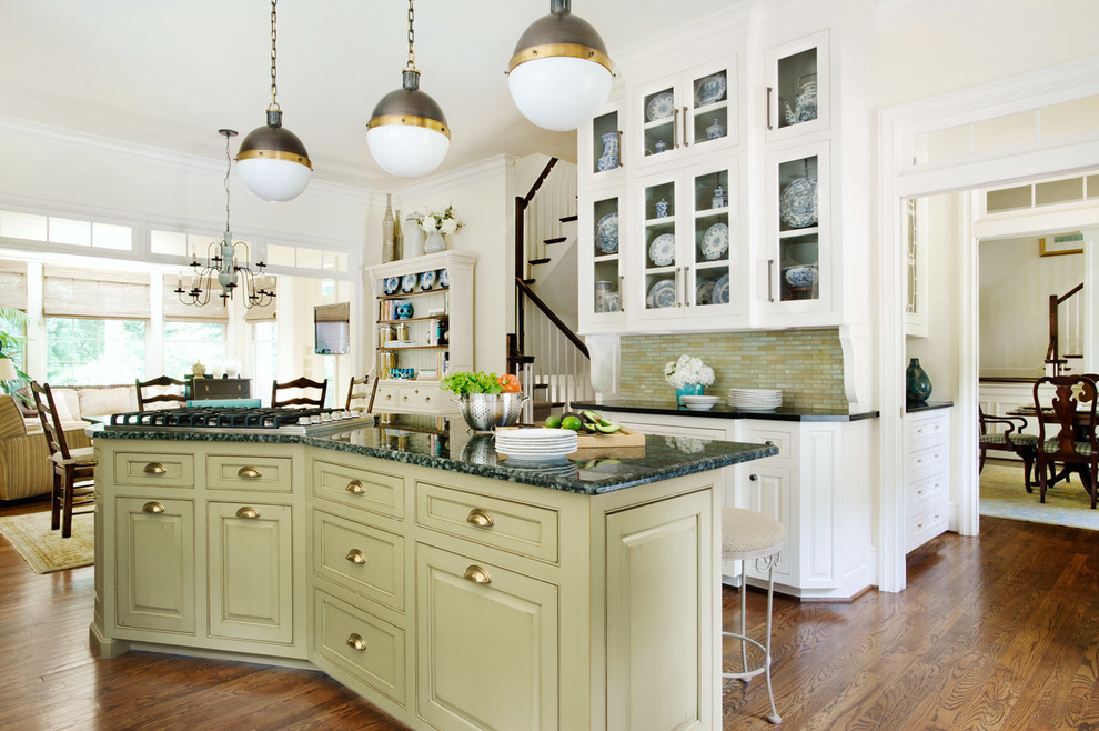 Klassisk inredning av ett kök, med en köksö, gröna skåp, granitbänkskiva, flerfärgad stänkskydd, en undermonterad diskho, stänkskydd i mosaik, rostfria vitvaror, mellanmörkt trägolv, brunt golv och luckor med profilerade fronter