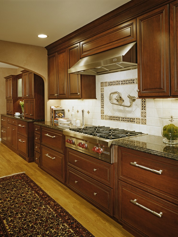 Large elegant galley light wood floor and brown floor eat-in kitchen photo in Detroit with an undermount sink, raised-panel cabinets, medium tone wood cabinets, granite countertops, white backsplash, ceramic backsplash, stainless steel appliances, an island and black countertops