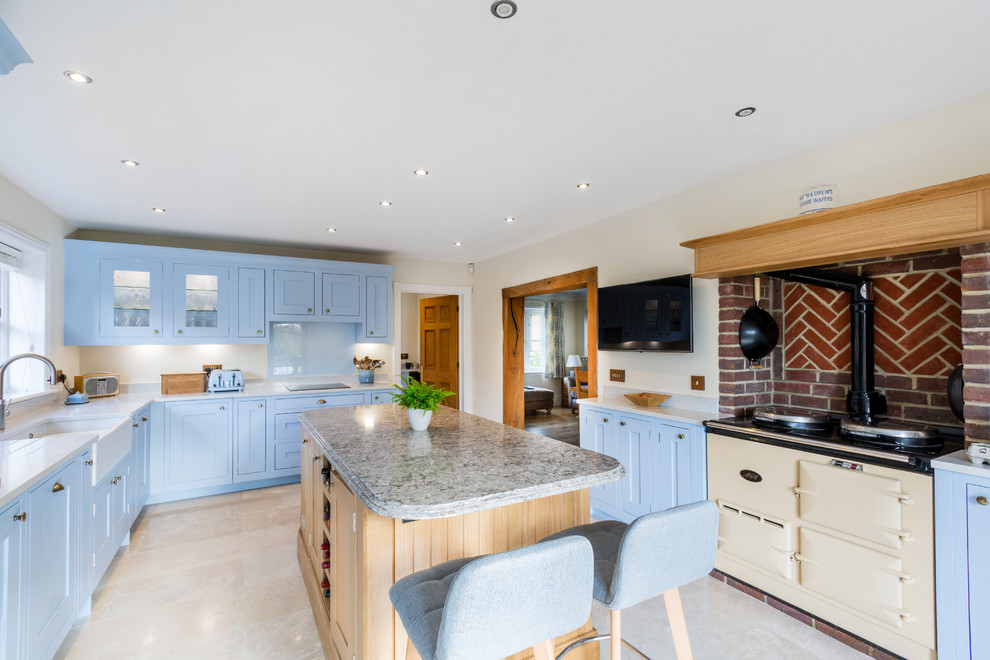 Inspiration for a classic grey and cream u-shaped enclosed kitchen in Surrey with shaker cabinets, blue cabinets, quartz worktops, blue splashback, an island, a belfast sink, glass sheet splashback, coloured appliances, beige floors and grey worktops.