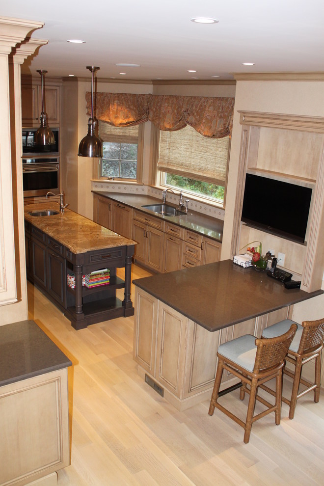 This is an example of a large traditional kitchen/diner in Boston with a submerged sink, recessed-panel cabinets, distressed cabinets, beige splashback, mosaic tiled splashback, stainless steel appliances, light hardwood flooring and an island.