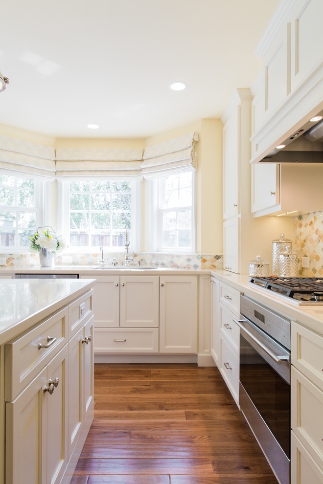 This is an example of a medium sized traditional l-shaped open plan kitchen in San Francisco with a submerged sink, shaker cabinets, white cabinets, engineered stone countertops, yellow splashback, stone tiled splashback, stainless steel appliances, medium hardwood flooring and an island.