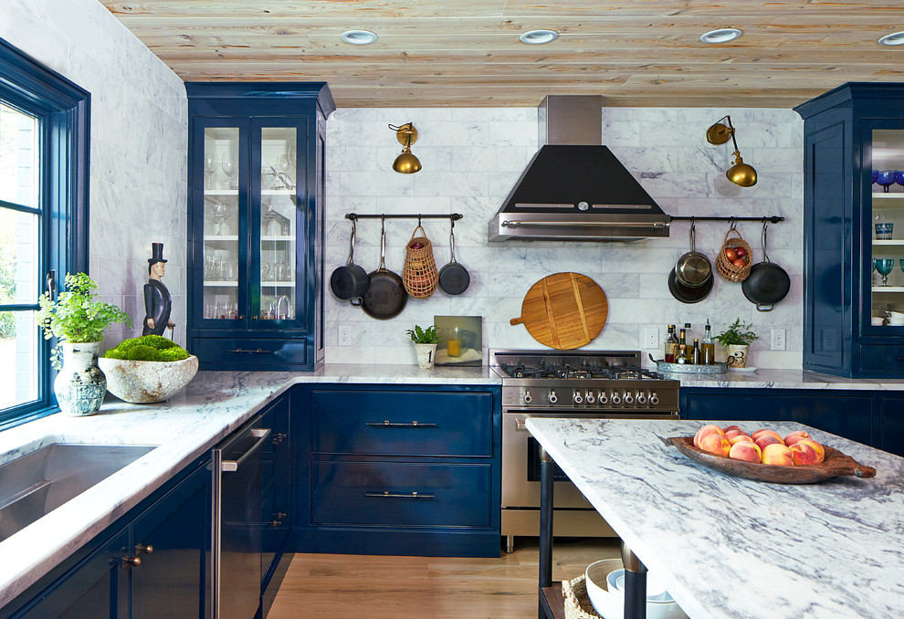 Foto di una cucina classica con lavello sottopiano, ante blu, top in marmo, paraspruzzi bianco, paraspruzzi con piastrelle in pietra, elettrodomestici in acciaio inossidabile, parquet chiaro e ante di vetro