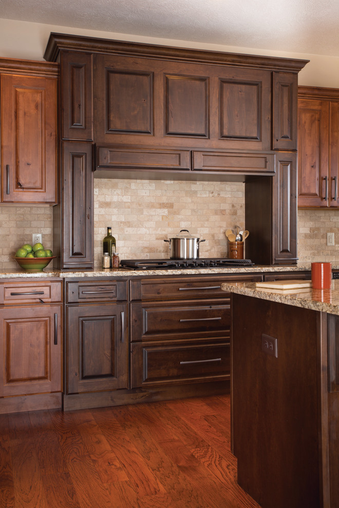 Inspiration for a mid-sized timeless l-shaped medium tone wood floor and brown floor open concept kitchen remodel in Other with raised-panel cabinets, dark wood cabinets, stainless steel appliances, an island, granite countertops, beige backsplash, an undermount sink and travertine backsplash