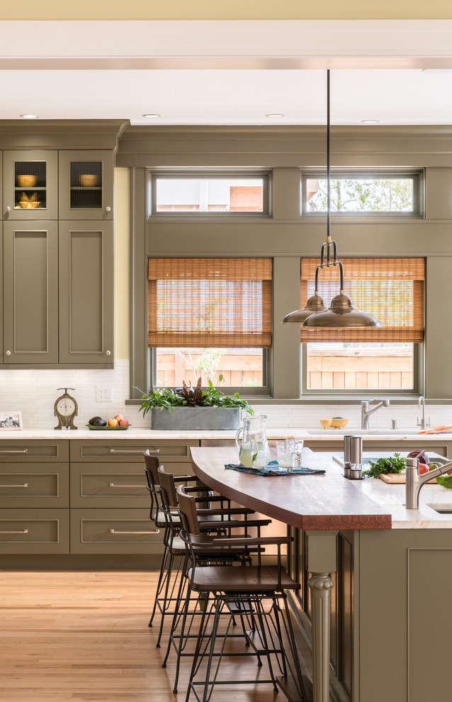 This is an example of a traditional kitchen in Denver with recessed-panel cabinets, green cabinets, white splashback, marble splashback, light hardwood flooring, an island and beige floors.
