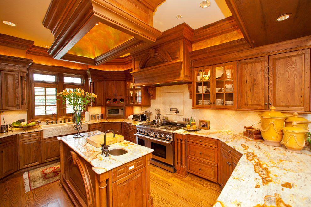 Example of a mid-sized classic u-shaped medium tone wood floor and brown floor enclosed kitchen design in Raleigh with a farmhouse sink, raised-panel cabinets, medium tone wood cabinets, marble countertops, beige backsplash, ceramic backsplash, stainless steel appliances and an island