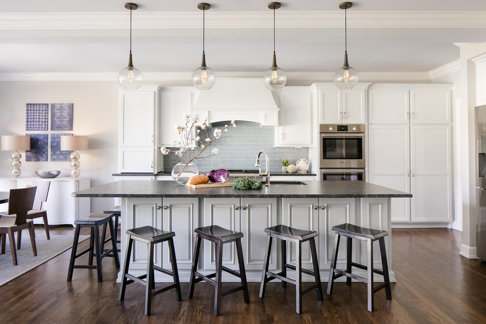 This is an example of a classic kitchen in Kansas City with a submerged sink, shaker cabinets, white cabinets, grey splashback, metro tiled splashback, stainless steel appliances, dark hardwood flooring, an island and brown floors.