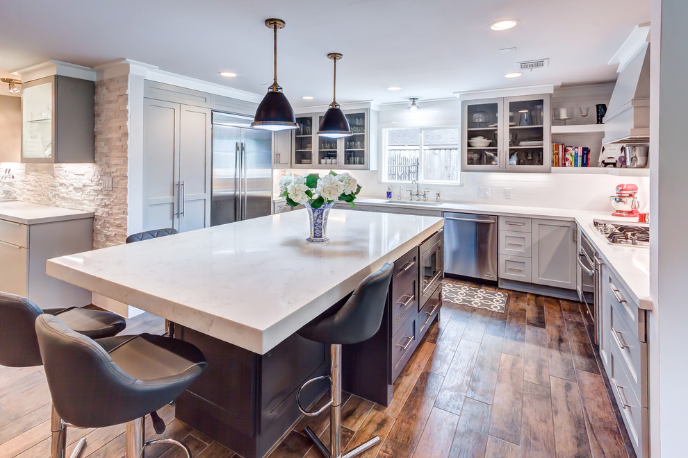 Example of a mid-sized transitional u-shaped porcelain tile and brown floor kitchen design in Houston with an undermount sink, shaker cabinets, gray cabinets, quartz countertops, white backsplash, subway tile backsplash, stainless steel appliances and an island