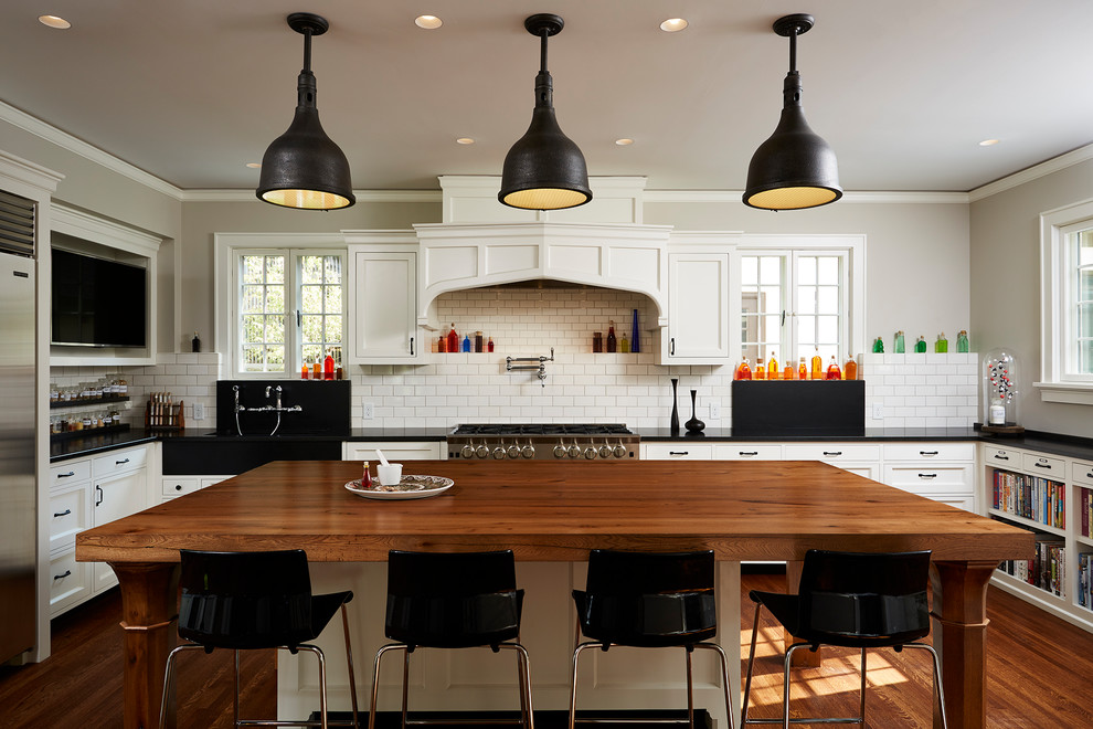Klassische Küche in U-Form mit Schrankfronten mit vertiefter Füllung, Arbeitsplatte aus Holz, Küchenrückwand in Weiß, Rückwand aus Metrofliesen, Küchengeräten aus Edelstahl, braunem Holzboden und Kücheninsel in Minneapolis