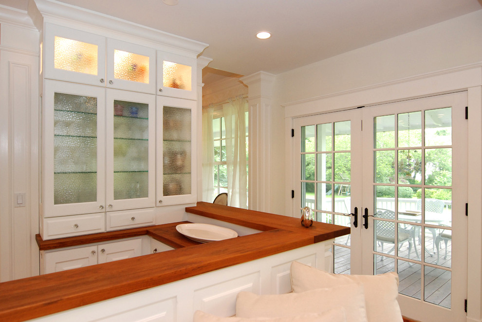 Exemple d'une cuisine chic avec un placard à porte vitrée, un plan de travail en bois et des portes de placard blanches.