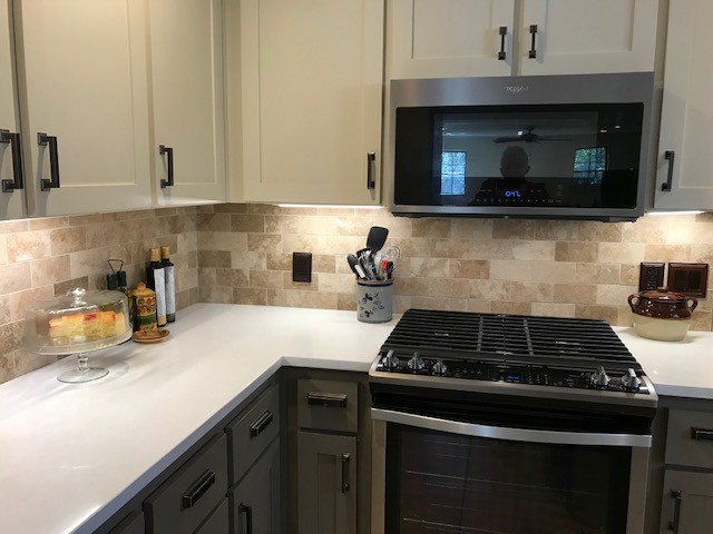 This is an example of a large traditional u-shaped kitchen/diner in Miami with a belfast sink, shaker cabinets, grey cabinets, engineered stone countertops, beige splashback, travertine splashback, stainless steel appliances, porcelain flooring, no island, beige floors and white worktops.