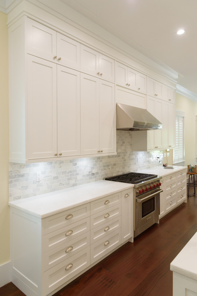 Bild på ett mellanstort vintage vit vitt u-kök, med en undermonterad diskho, skåp i shakerstil, vita skåp, bänkskiva i kvarts, grått stänkskydd, stänkskydd i tunnelbanekakel, rostfria vitvaror, mellanmörkt trägolv, en köksö och brunt golv