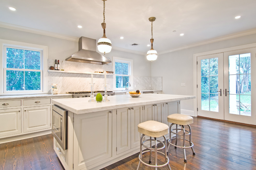 Klassisk inredning av ett kök, med luckor med upphöjd panel, vita skåp, vitt stänkskydd, stänkskydd i sten och rostfria vitvaror