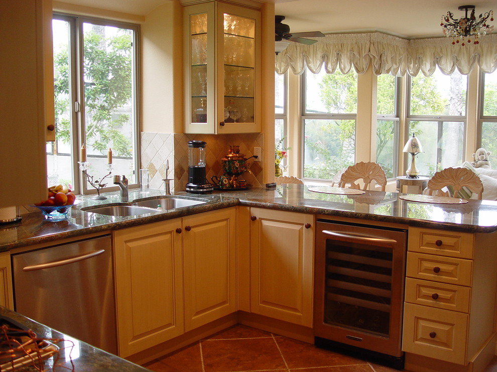 This is an example of a medium sized traditional u-shaped kitchen/diner in San Francisco with stainless steel appliances, a double-bowl sink, raised-panel cabinets, light wood cabinets, granite worktops, beige splashback, ceramic splashback, ceramic flooring, a breakfast bar and brown floors.