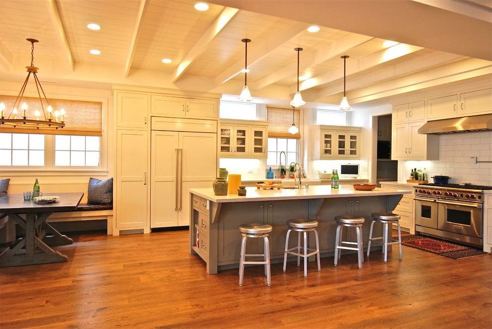Свежая идея для дизайна: кухня-гостиная в классическом стиле с техникой под мебельный фасад, стеклянными фасадами, белыми фасадами, белым фартуком и столешницей из кварцевого агломерата - отличное фото интерьера