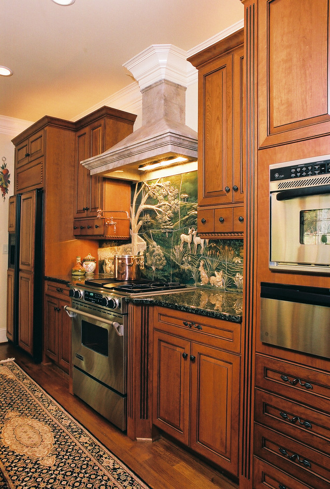 Diseño de cocina tradicional con armarios con paneles con relieve, puertas de armario de madera en tonos medios, salpicadero gris y electrodomésticos de acero inoxidable
