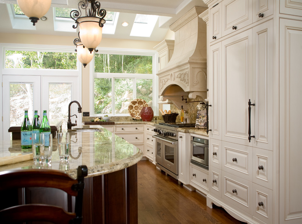 Foto på ett stort vintage kök, med en dubbel diskho, luckor med upphöjd panel, vita skåp, granitbänkskiva, beige stänkskydd, stänkskydd i sten, rostfria vitvaror, mellanmörkt trägolv och en köksö