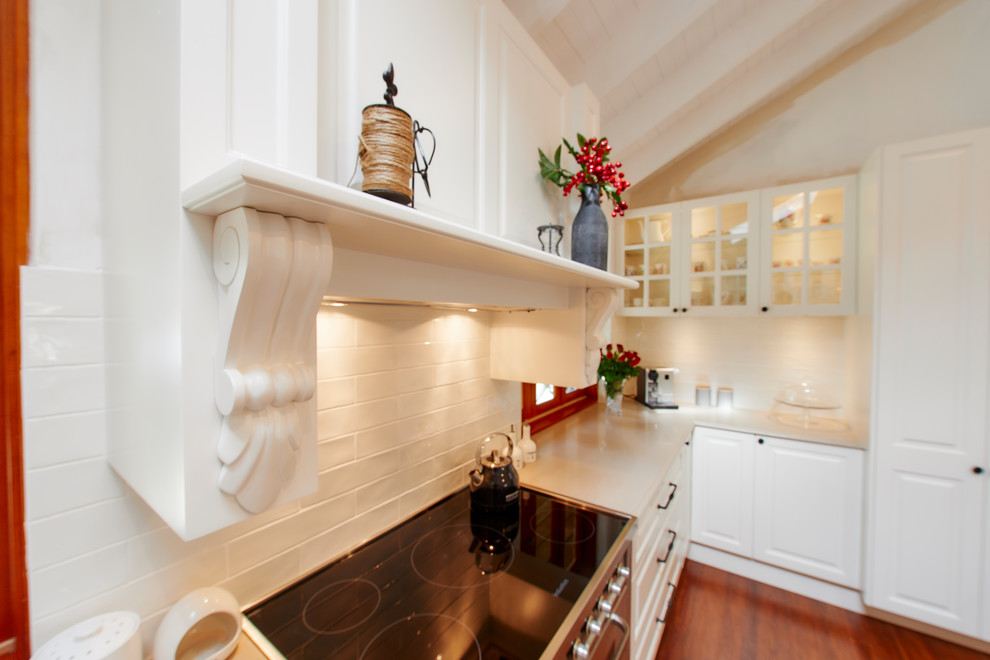 Idéer för att renovera ett stort vintage u-kök, med en undermonterad diskho, luckor med infälld panel, vita skåp, bänkskiva i kvarts, vitt stänkskydd, stänkskydd i travertin, vita vitvaror, mellanmörkt trägolv, en köksö och flerfärgat golv