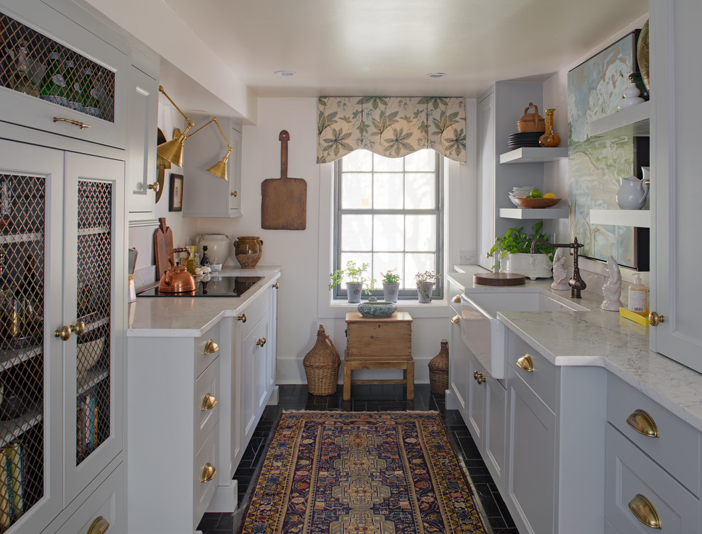 Exemple d'une cuisine parallèle chic avec un plan de travail en quartz modifié, un placard avec porte à panneau encastré, des portes de placard blanches, îlot et un sol noir.