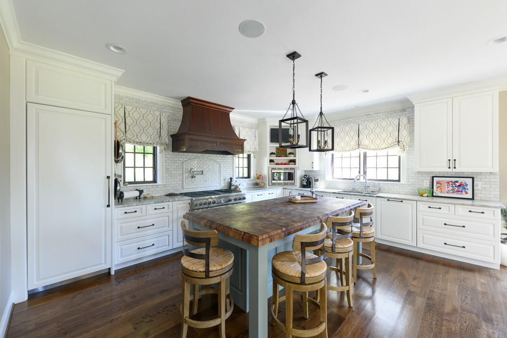 Example of a classic l-shaped dark wood floor and brown floor kitchen design in Other with an undermount sink, raised-panel cabinets, white cabinets, wood countertops, white backsplash, stainless steel appliances, an island and brown countertops