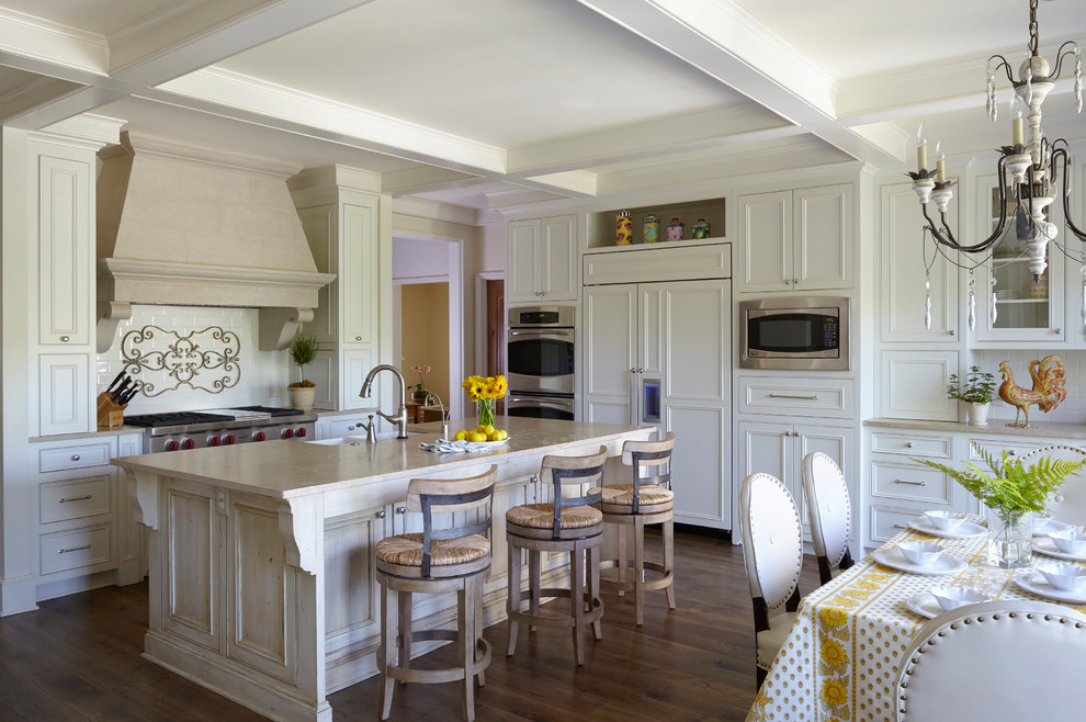 Inredning av ett klassiskt kök, med luckor med infälld panel, vita skåp, vitt stänkskydd, stänkskydd i tunnelbanekakel, integrerade vitvaror, mörkt trägolv, en köksö och brunt golv