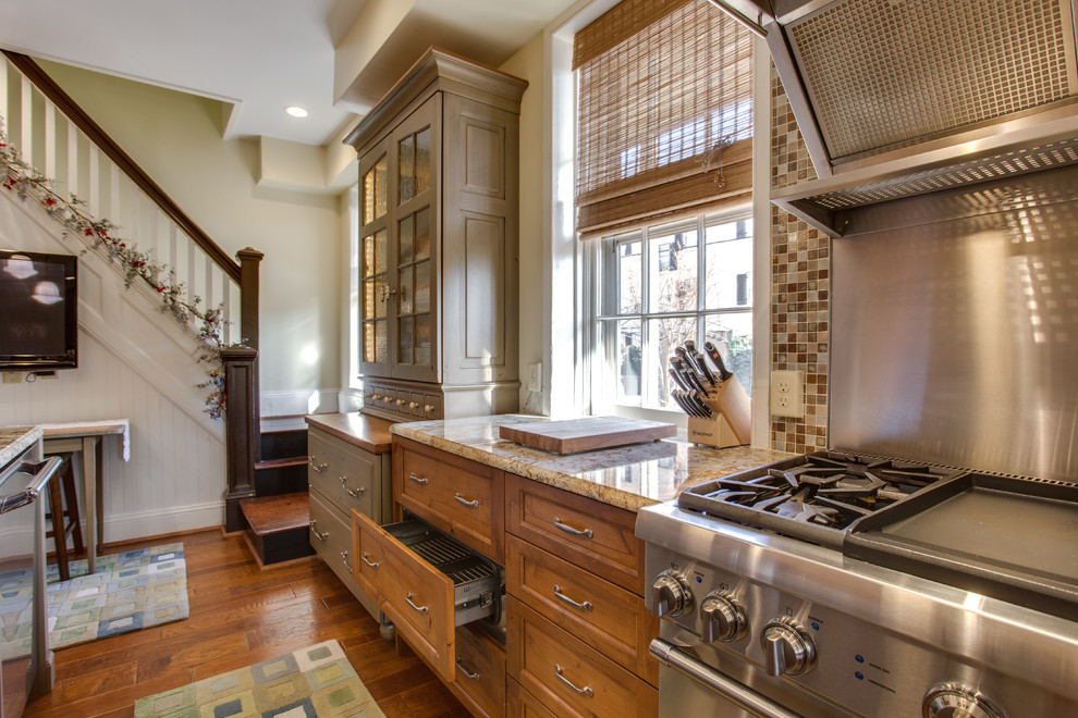 Small traditional l-shaped enclosed kitchen in DC Metro with a belfast sink, raised-panel cabinets, medium wood cabinets, granite worktops, stainless steel appliances, medium hardwood flooring and an island.