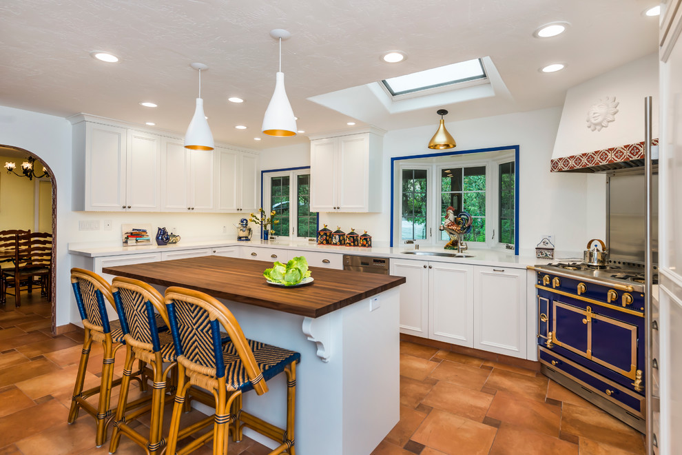 Large mediterranean u-shaped open plan kitchen in San Francisco with a double-bowl sink, recessed-panel cabinets, white cabinets, composite countertops, integrated appliances, terracotta flooring, an island, brown floors and white worktops.