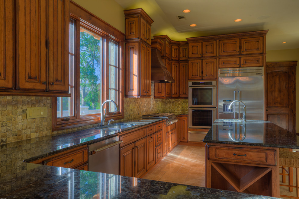Klassisk inredning av ett kök, med luckor med upphöjd panel, skåp i slitet trä, flerfärgad stänkskydd och rostfria vitvaror