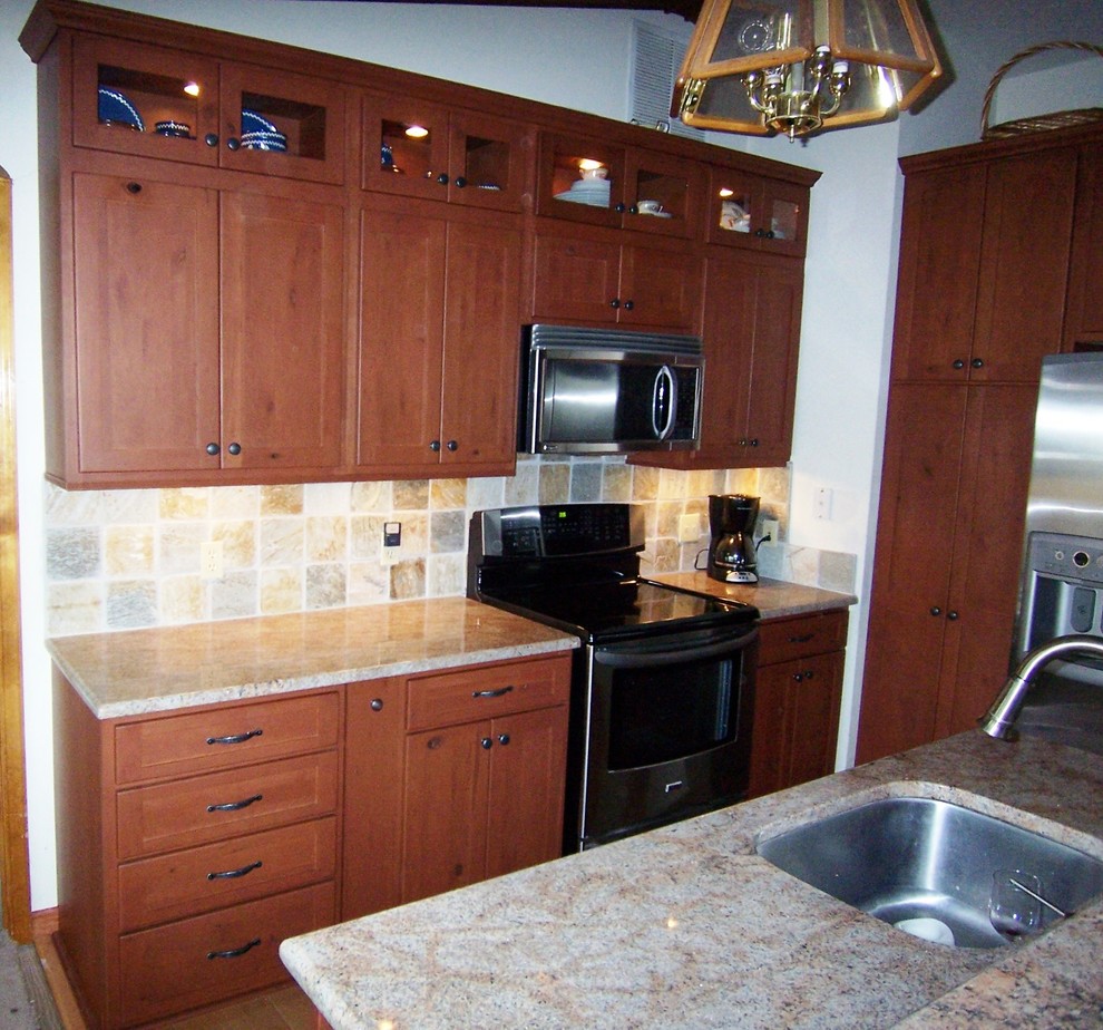 This is an example of a large traditional l-shaped kitchen/diner in DC Metro with a built-in sink, flat-panel cabinets, medium wood cabinets, granite worktops, beige splashback, stone tiled splashback, black appliances, medium hardwood flooring and an island.