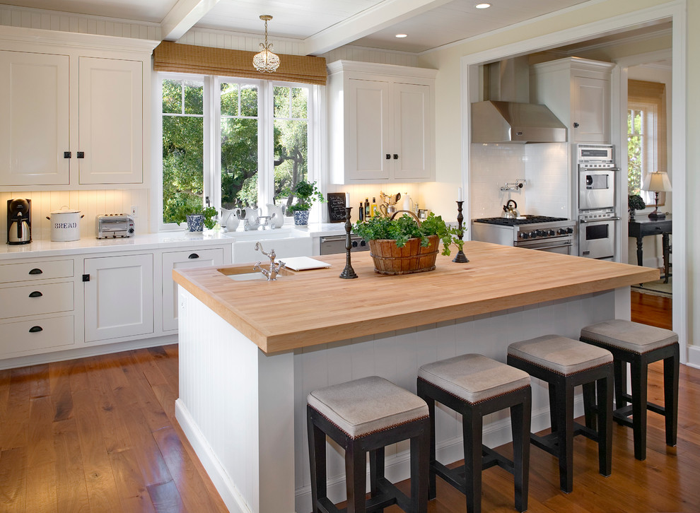 This is an example of a classic kitchen in Santa Barbara with a belfast sink, shaker cabinets, white cabinets, wood worktops, white splashback and stainless steel appliances.